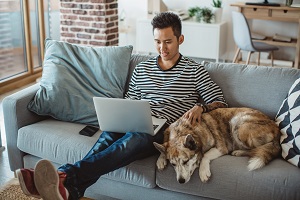 man sitting on couch on laptop with dog